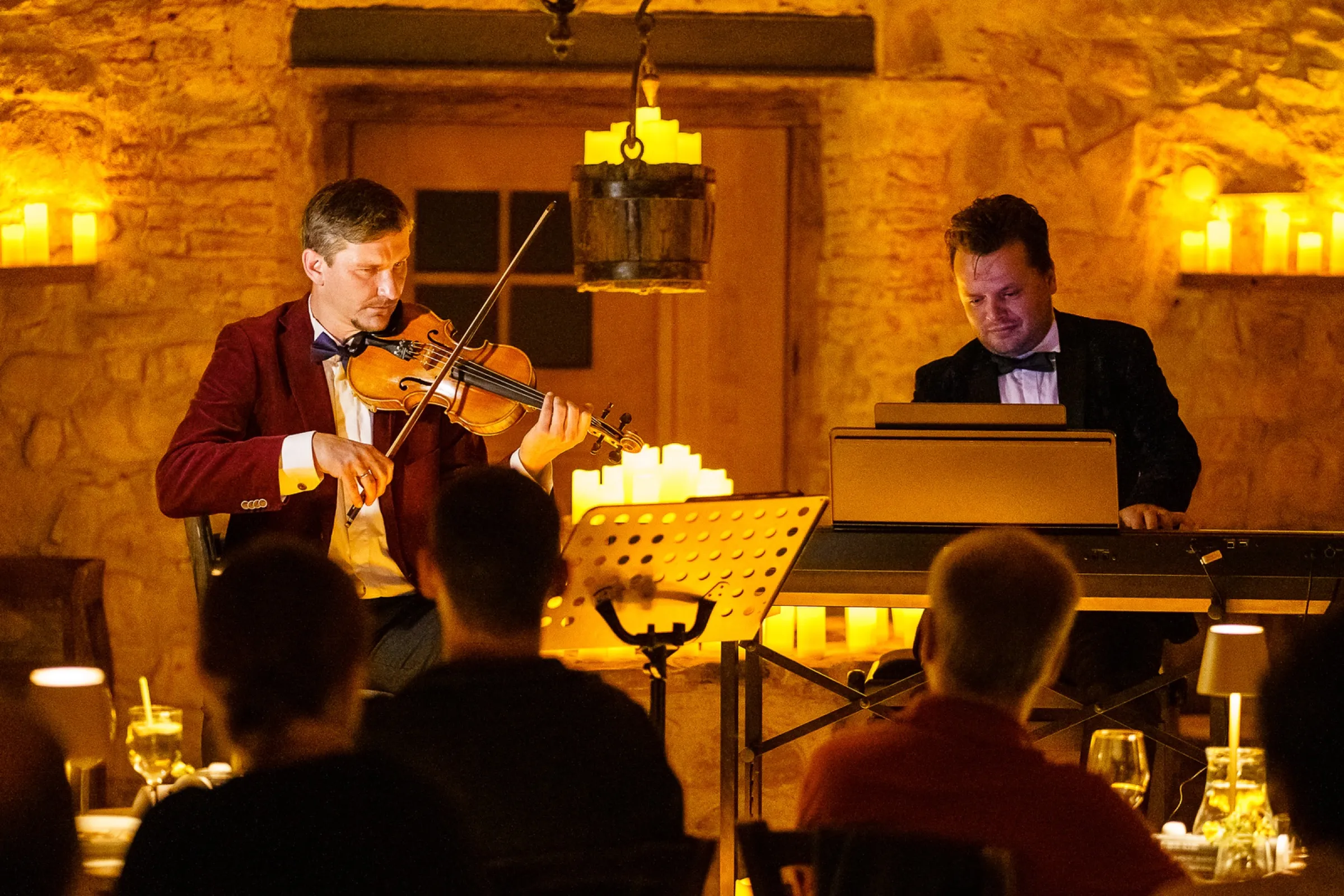 A violinist and pianist performing for guests in the candlelit Kálnoky Castle wine cellar