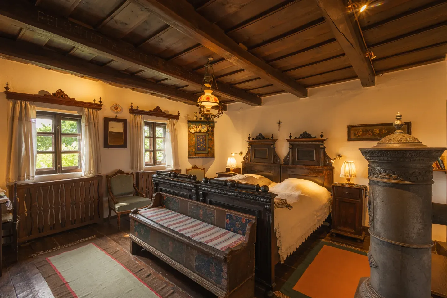 A traditional bedroom at Count Kálnoky’s Guesthouses, with carved wooden furniture and a tiled stove.